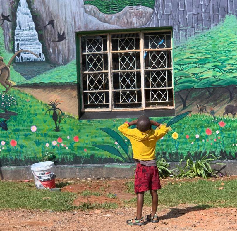 A child standing before a large hand-painted community mural in Zimbabwe